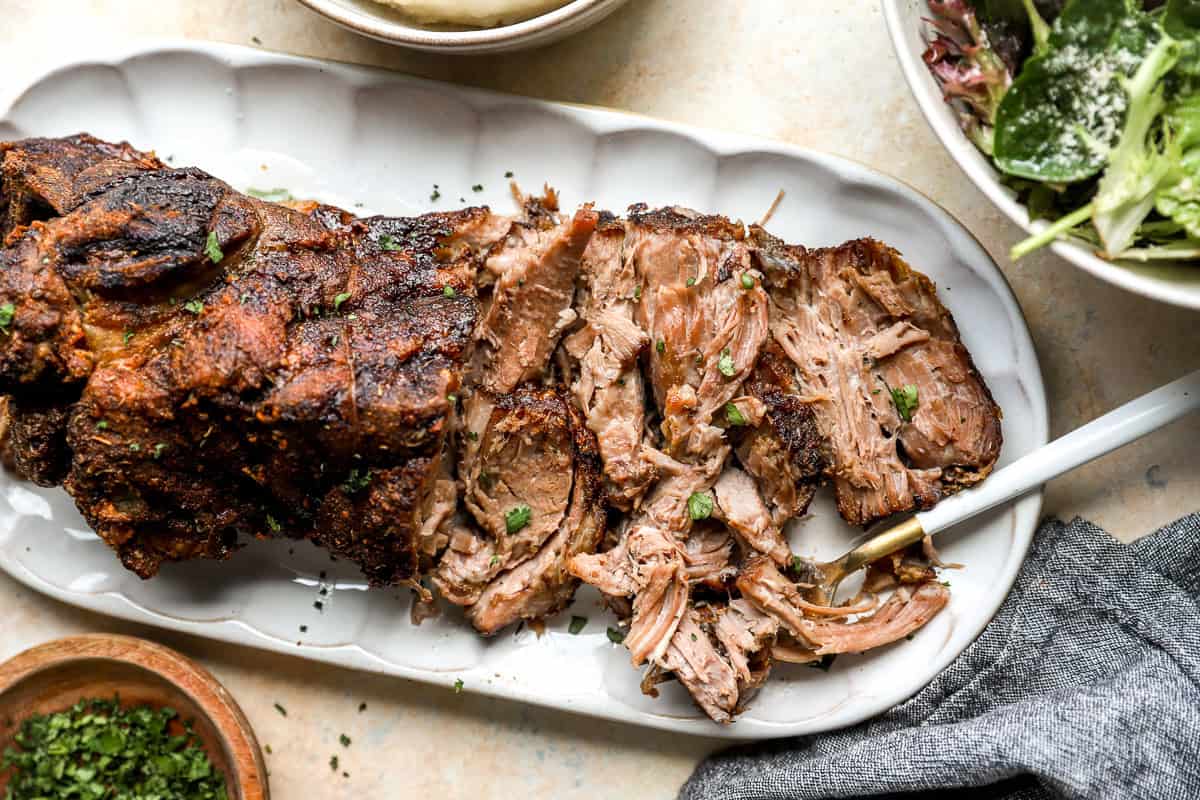 Tender roasted pork shoulder sliced and shredded on a serving platter with crispy edges.