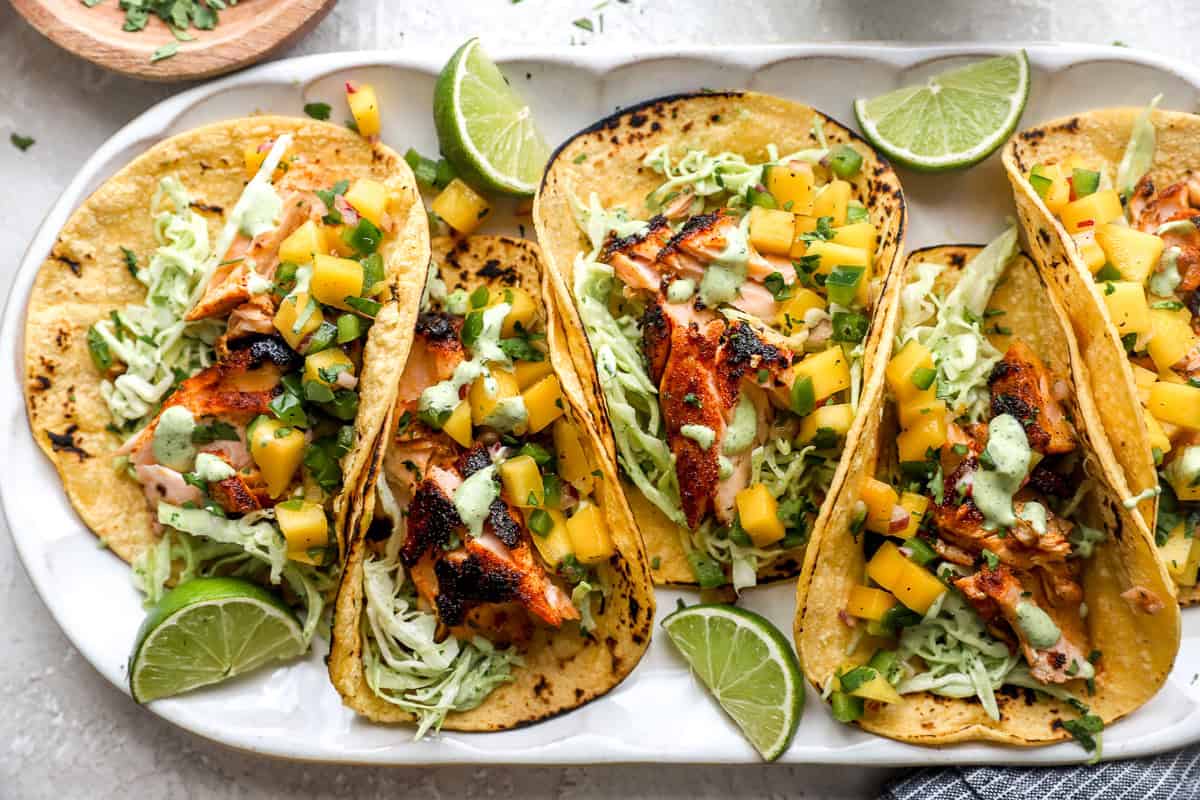 Platter of salmon tacos topped with mango salsa, cilantro lime slaw, and creamy cilantro dressing.