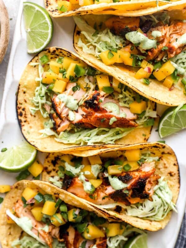 Salmon tacos topped with mango salsa and cilantro lime slaw on charred corn tortillas with fresh lime wedges.