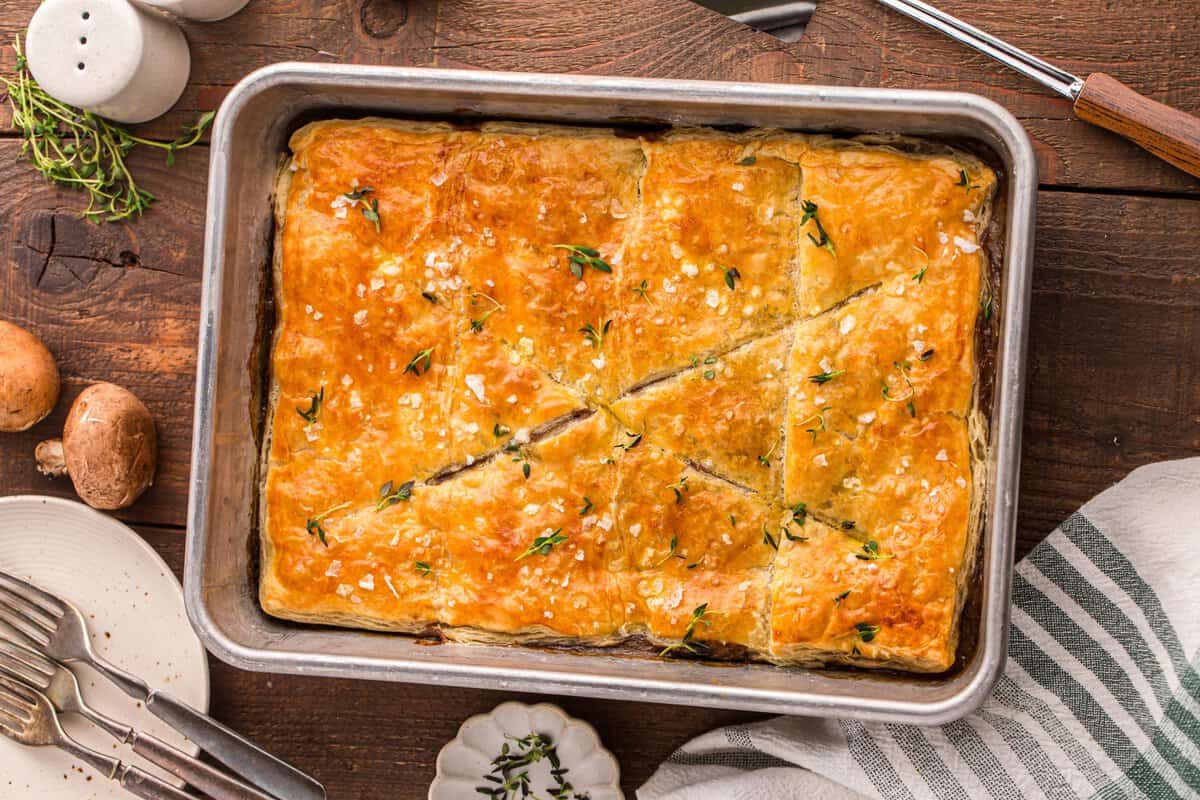Beef Wellington pot pie bake fresh from the oven in a metal pan with golden flaky pastry, flaky salt, and fresh thyme