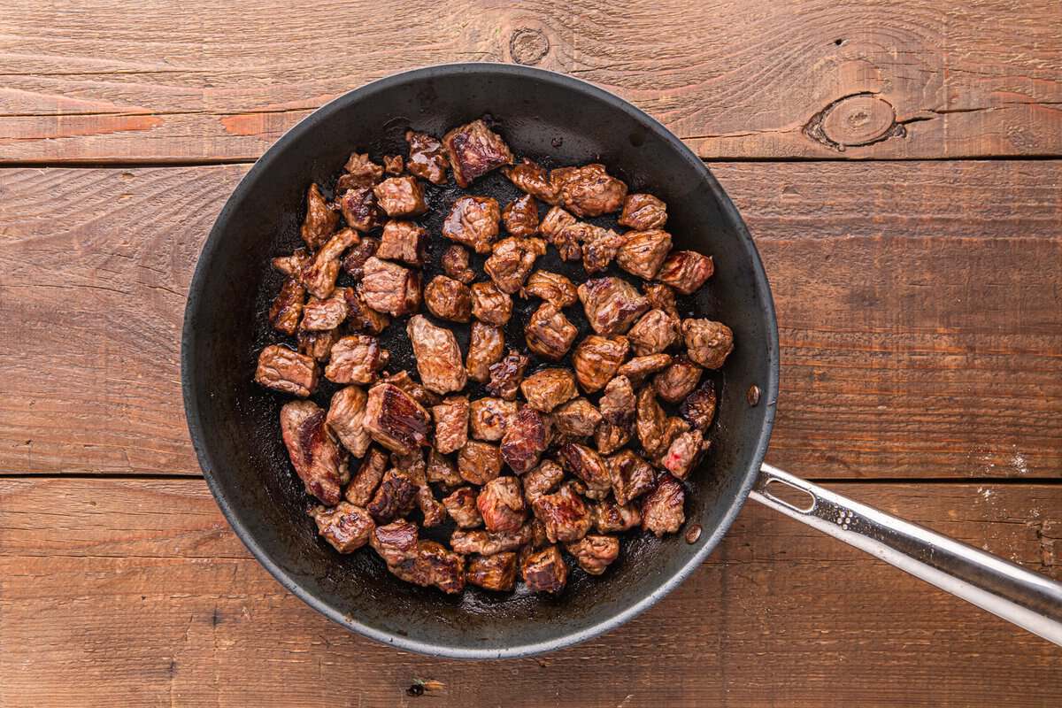 Seared beef sirloin pieces with deep brown crust in a dark skillet on a wood surface