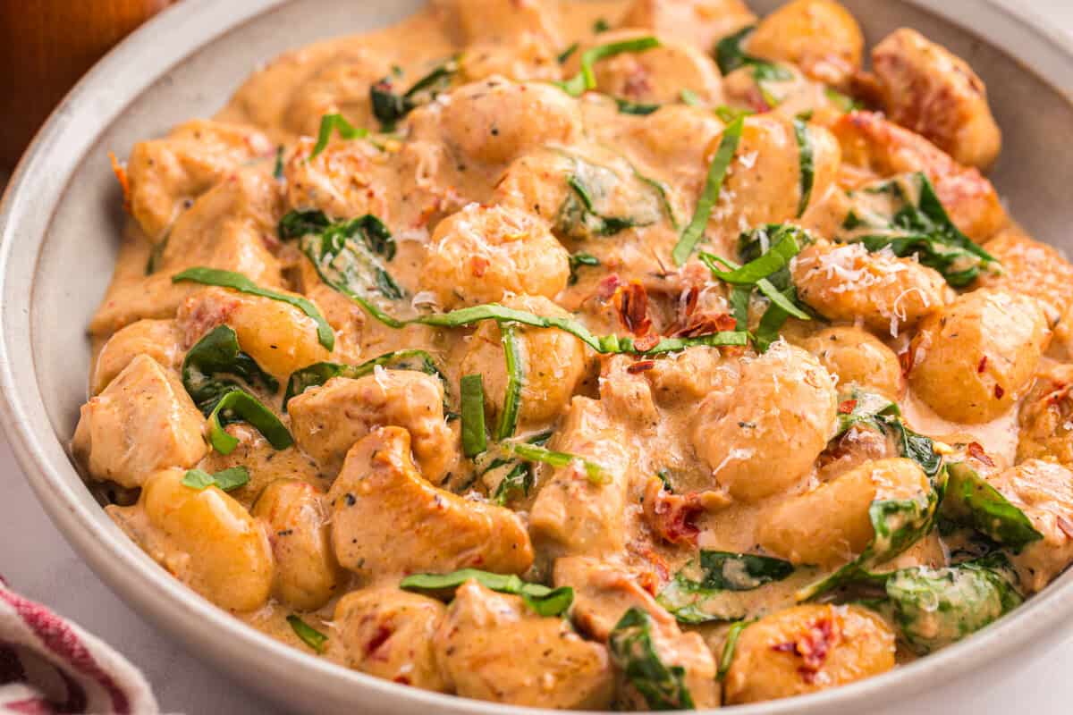 Marry me chicken gnocchi served in a bowl topped with fresh basil, grated parmesan, and sun-dried tomatoes in a creamy sauce.