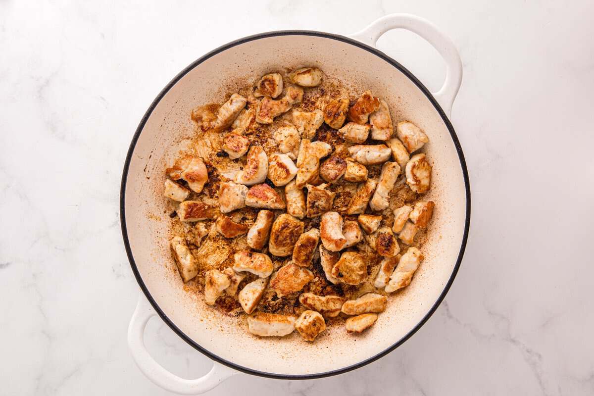 Golden seared chicken pieces in a white skillet with browned bits on the bottom of the pan.