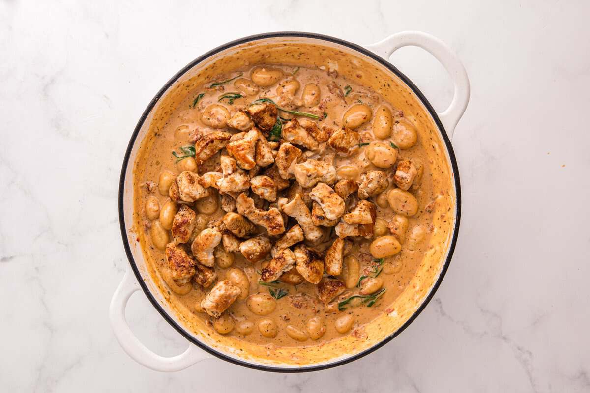 Seared chicken pieces returned to the skillet on top of gnocchi and creamy sauce before stirring to combine.