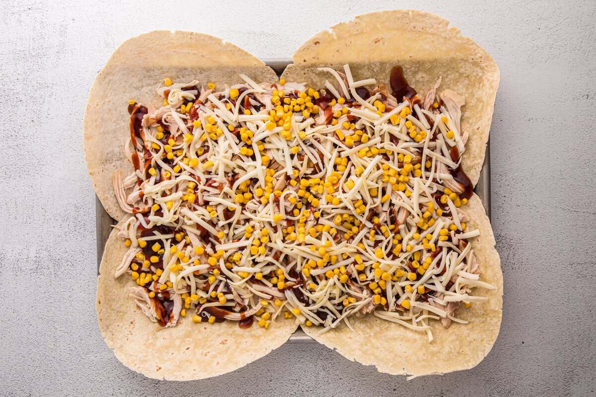 BBQ chicken topped with shredded Monterey Jack cheese and sweet corn on tortillas before assembling the crunchwrap.