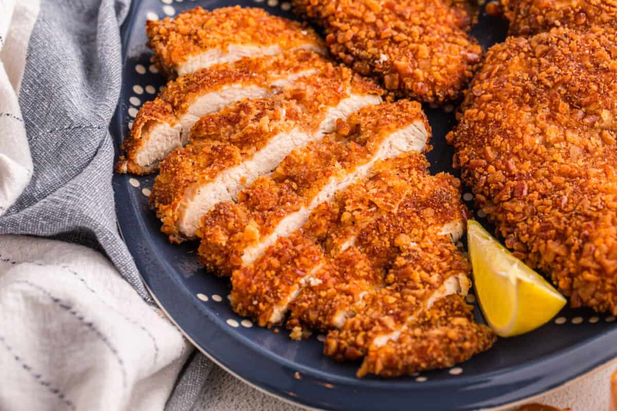 Sliced pretzel crusted chicken cutlet on a dark blue platter showing the juicy white interior and crispy golden crust