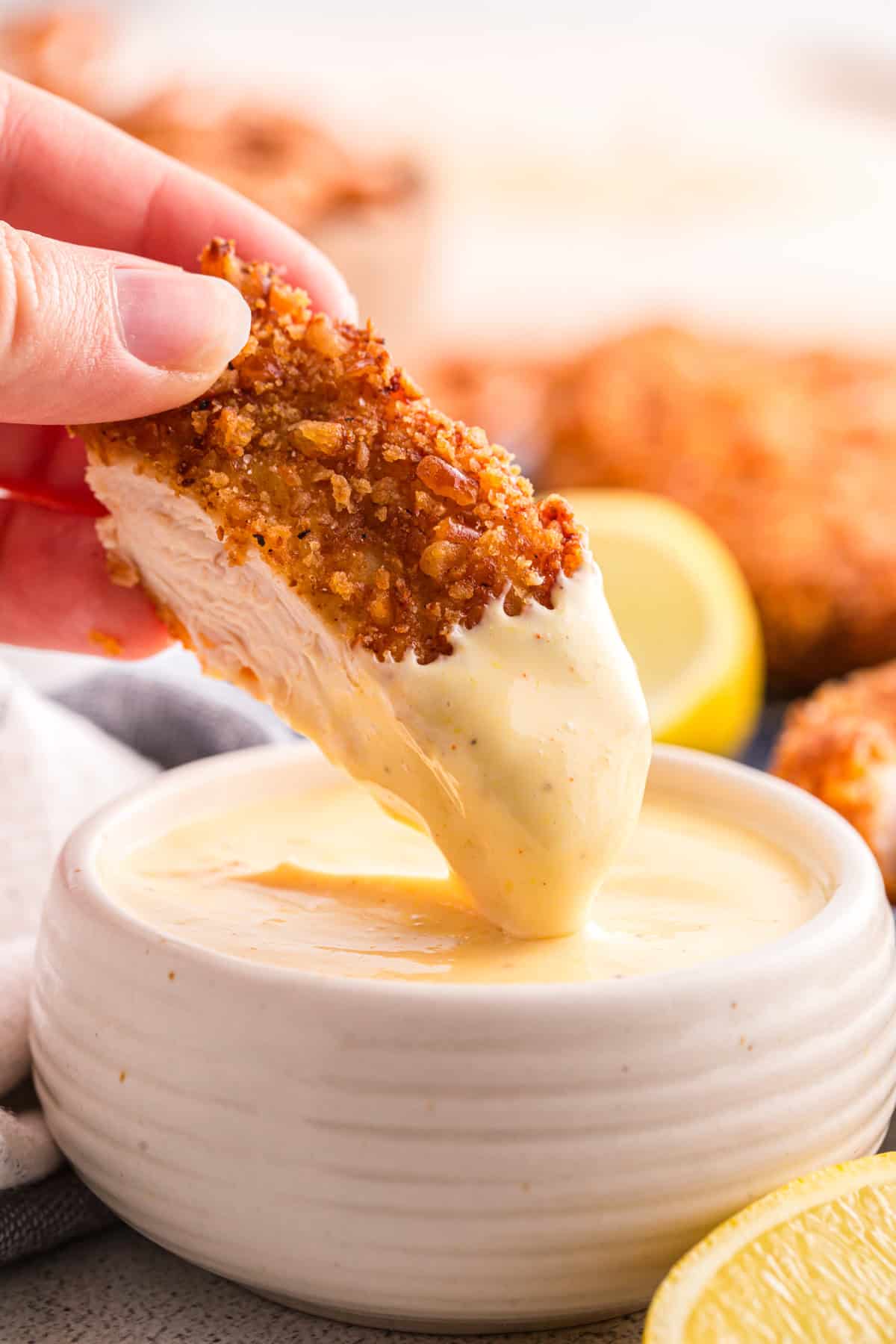 Hand dipping a slice of pretzel crusted chicken cutlet into a small bowl of creamy honey mustard dipping sauce