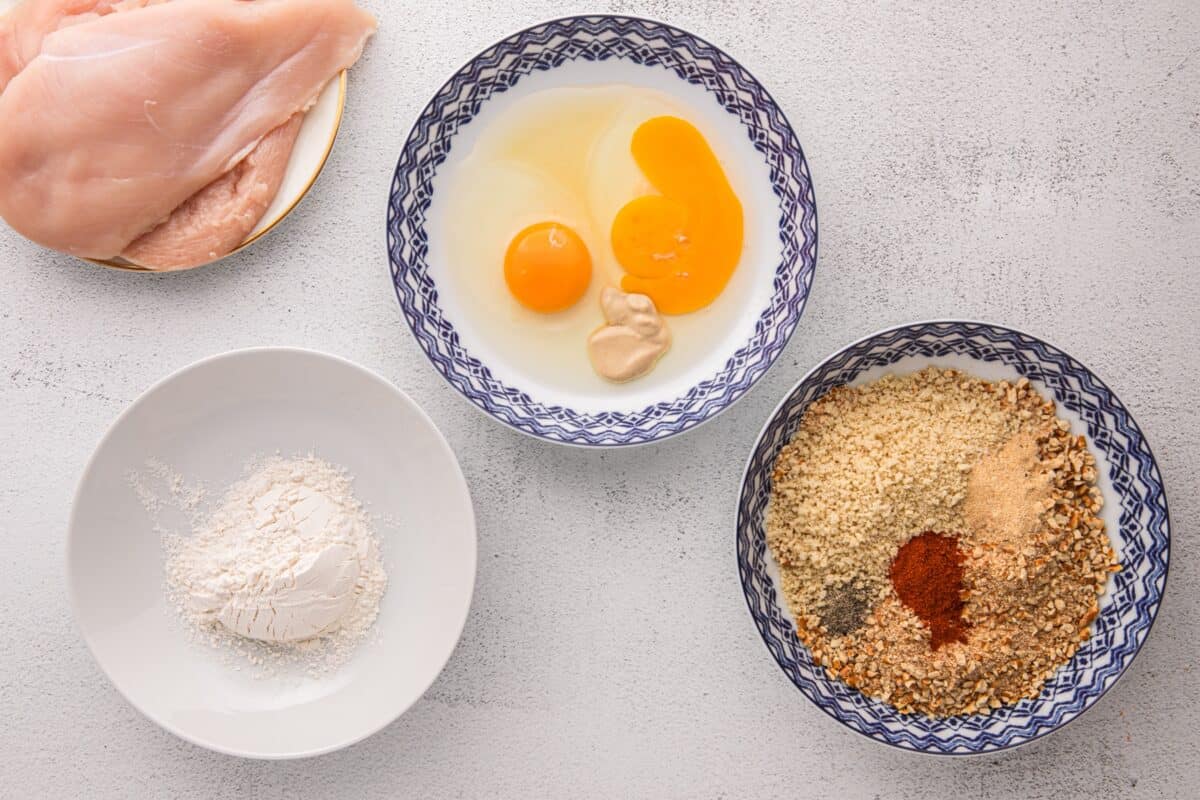 Three bowls showing the dredging station setup with flour, egg wash, and pretzel panko coating mixture with spices