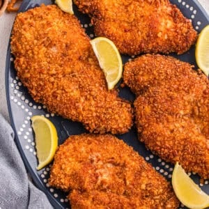 Pretzel crusted chicken cutlets on a dark blue oval platter with lemon wedges and whole pretzels in the background