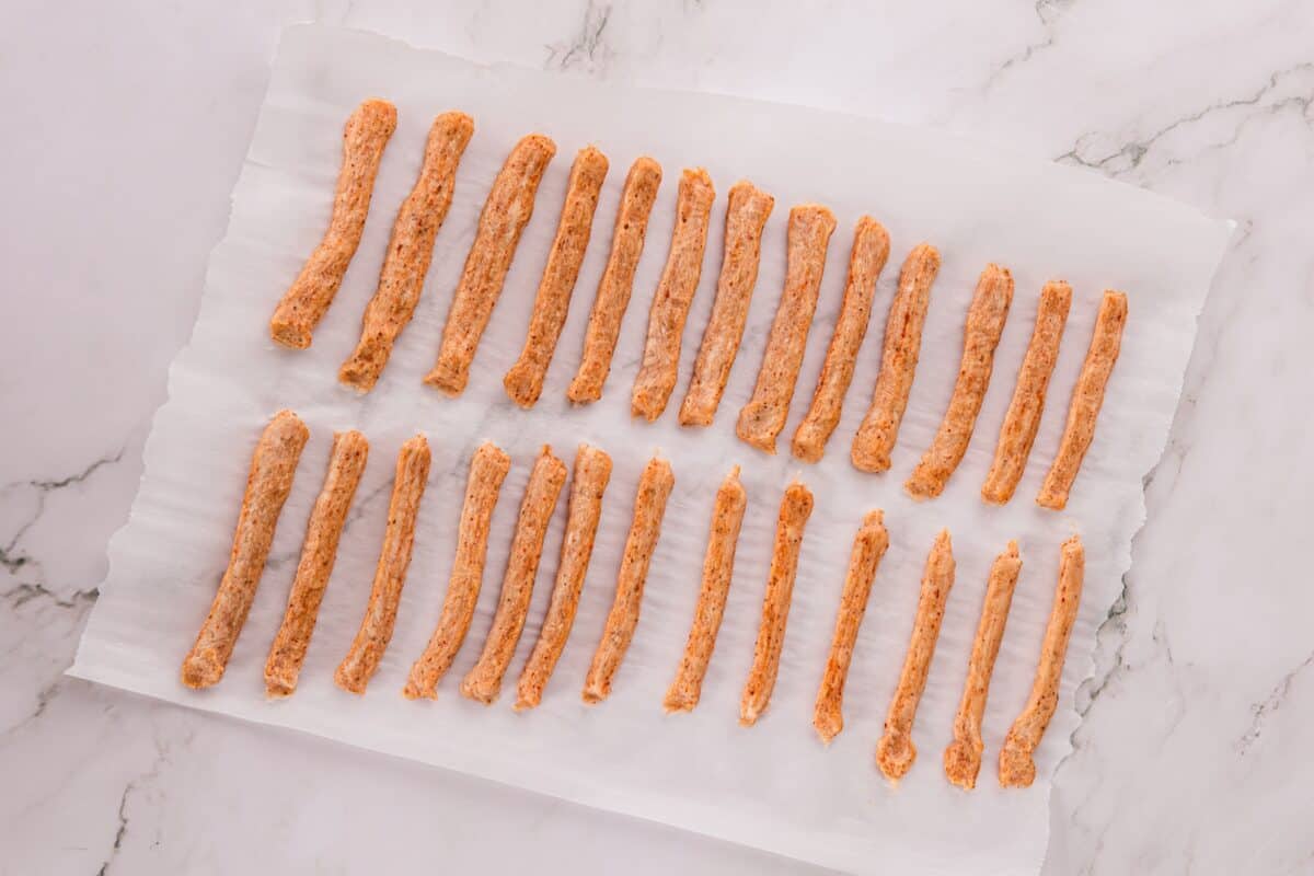 Overhead view of raw seasoned chicken fries shaped into strips and arranged in rows on parchment paper.