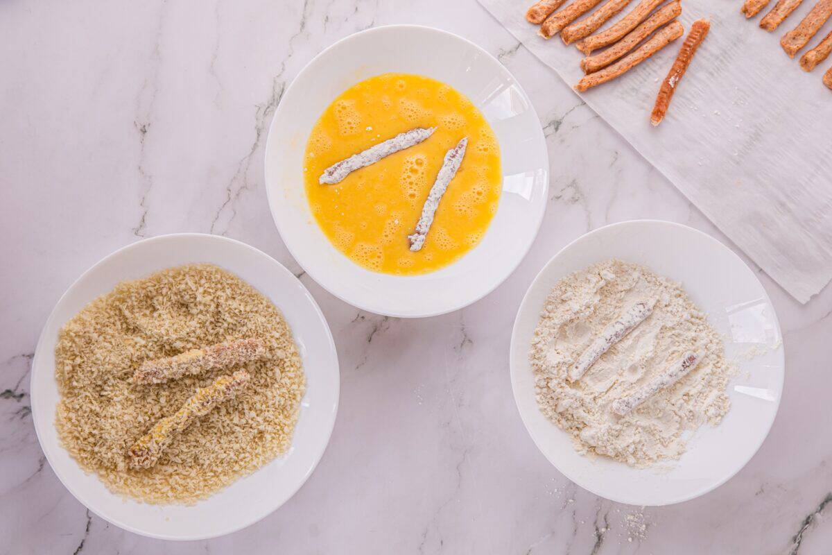 Overhead view of chicken fries being dredged in flour, egg, and panko breadcrumbs.