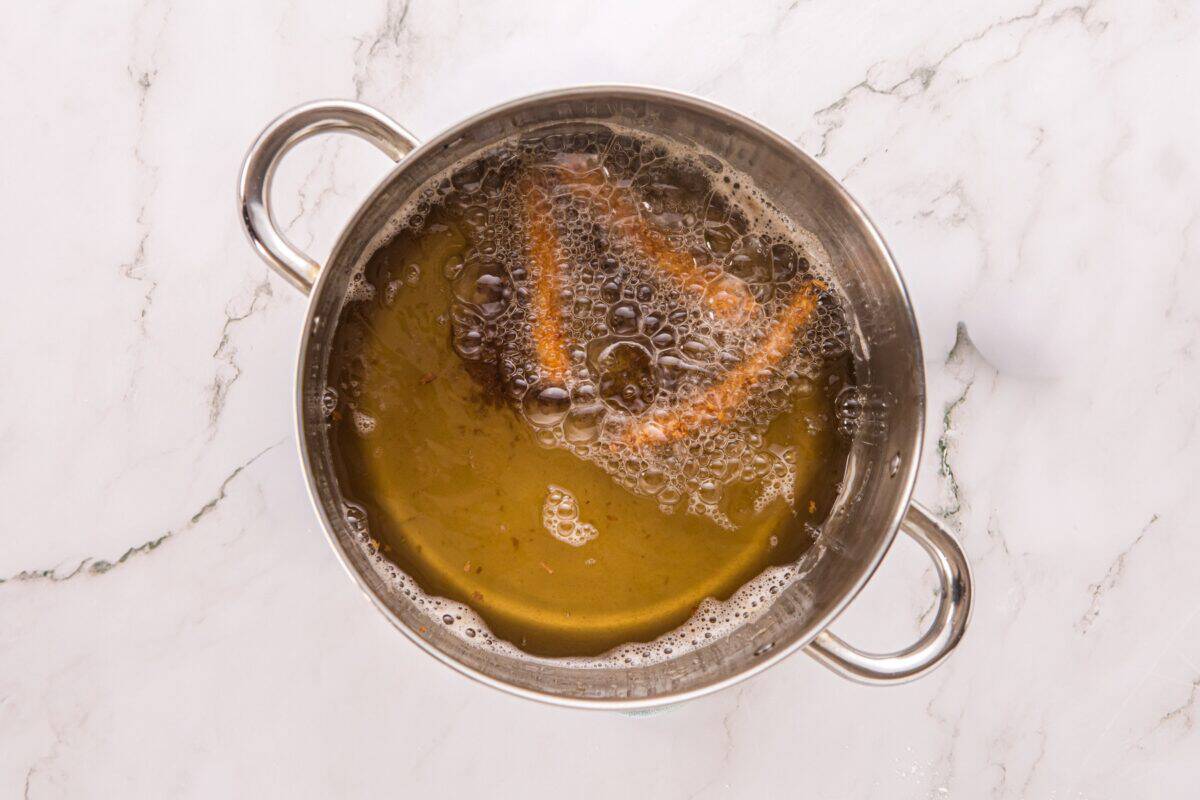 Overhead view of a breaded chicken fry frying in a pot of bubbling hot oil.