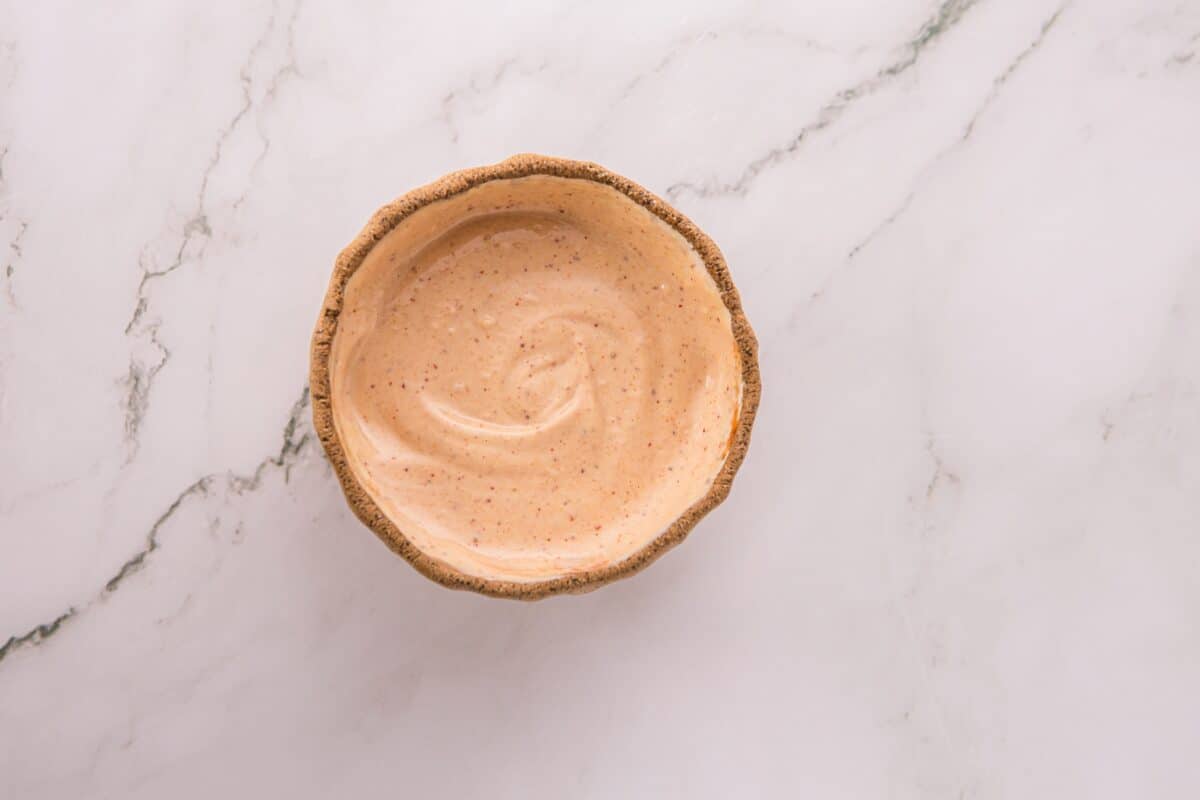 Overhead close-up of creamy orange dipping sauce in a small speckled ceramic bowl.
