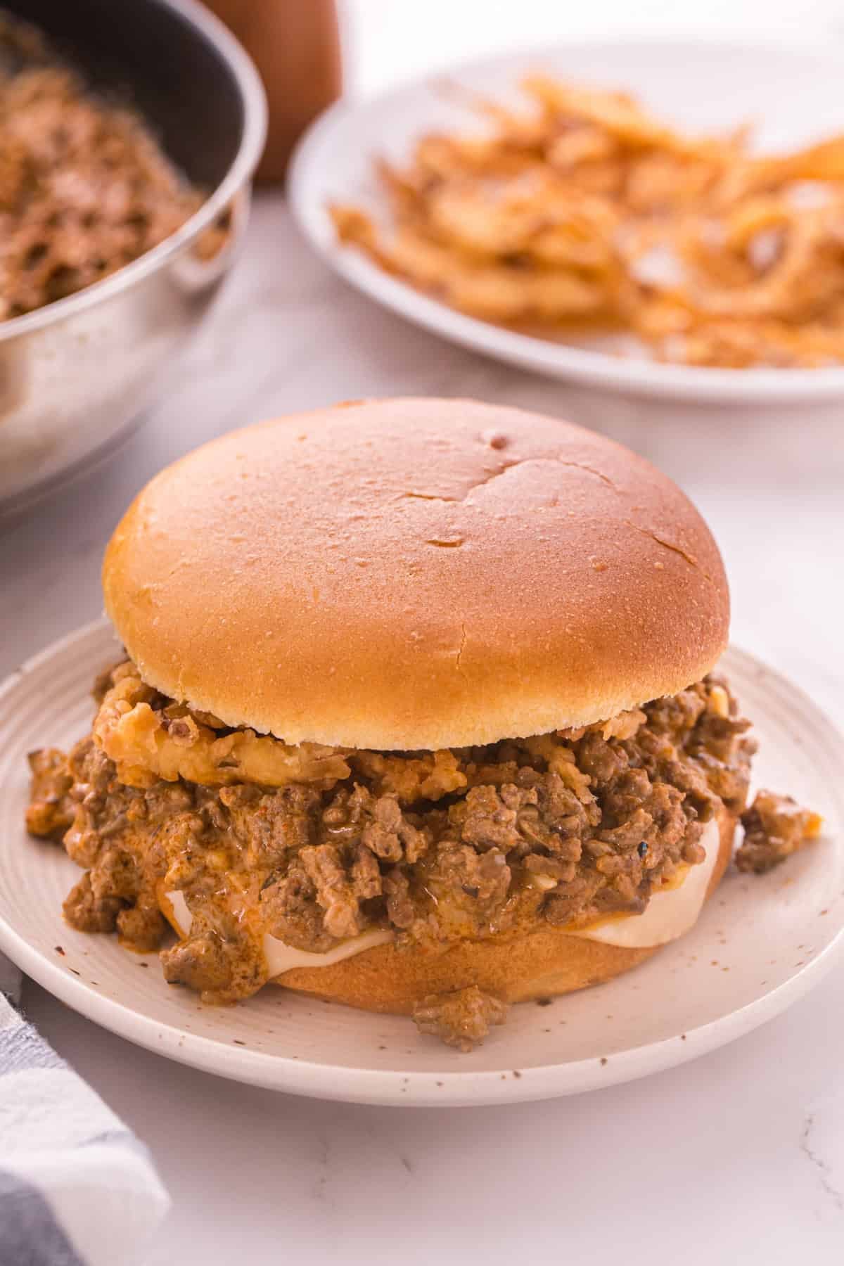 Beef Stroganoff Sloppy Joe sandwich on a brioche bun with melted Swiss cheese and crispy fried onions on a white plate