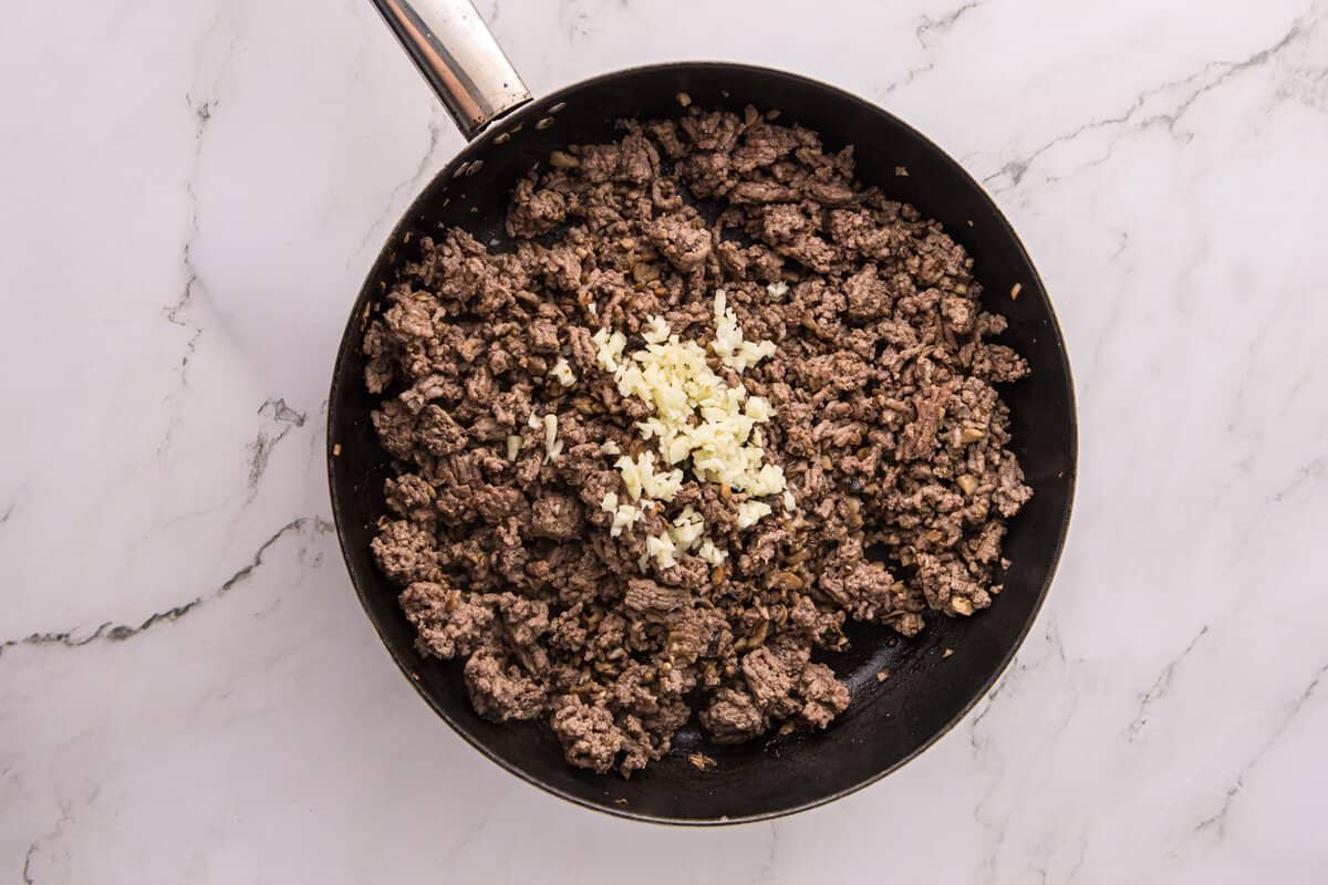Ground beef and browned mushrooms in a skillet with minced garlic added in the center