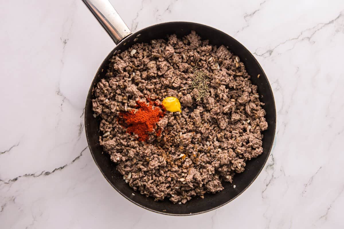 Beef and mushroom mixture in a skillet topped with paprika, Dijon mustard, and dried thyme before stirring