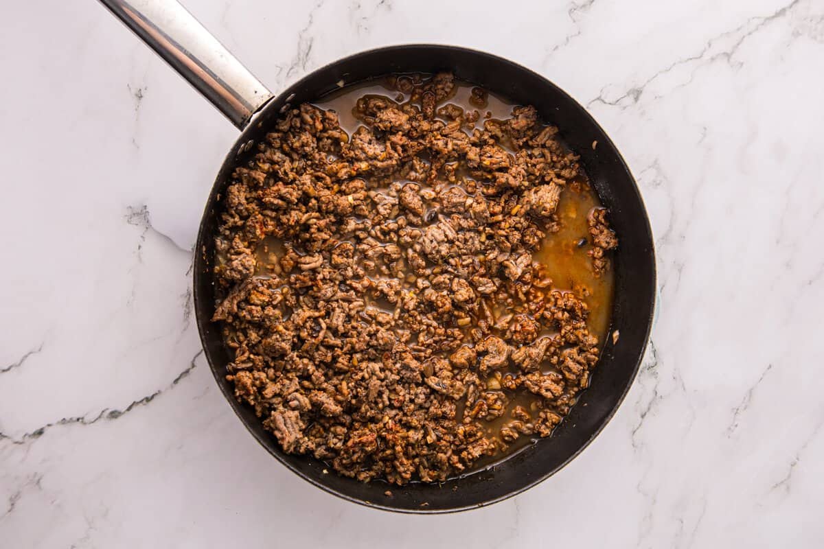 Beef stroganoff filling simmering in beef broth in a skillet before the sauce thickens