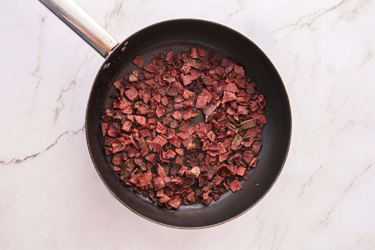 Chopped corned beef browning and crisping in a black skillet, ready to mix into the filling.