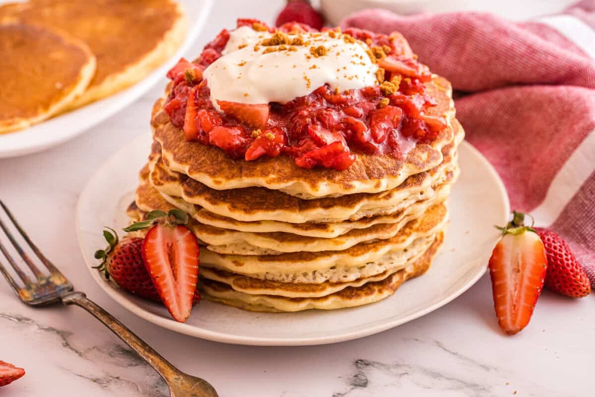 Plated strawberry cheesecake pancakes, showing topped with strawberry sauce and whipped cream