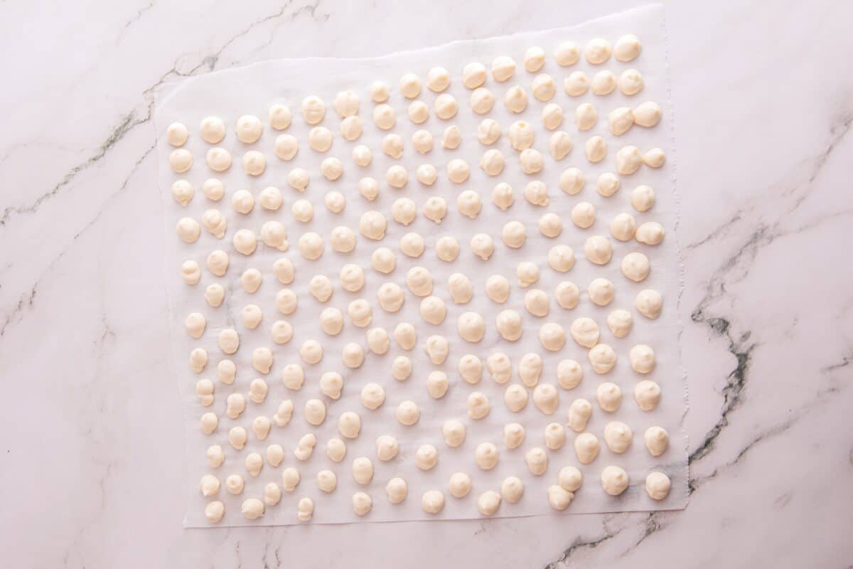 Rows of small cream cheese dollops piped onto parchment paper before freezing into cheesecake bites
