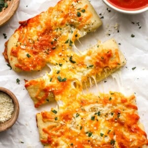 Overhead shot of sliced stuffed cheesy bread with melted cheese pulling apart, next to a bowl of marinara sauce and grated parmesan