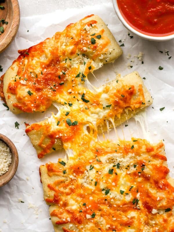 Overhead shot of sliced stuffed cheesy bread with melted cheese pulling apart, next to a bowl of marinara sauce and grated parmesan