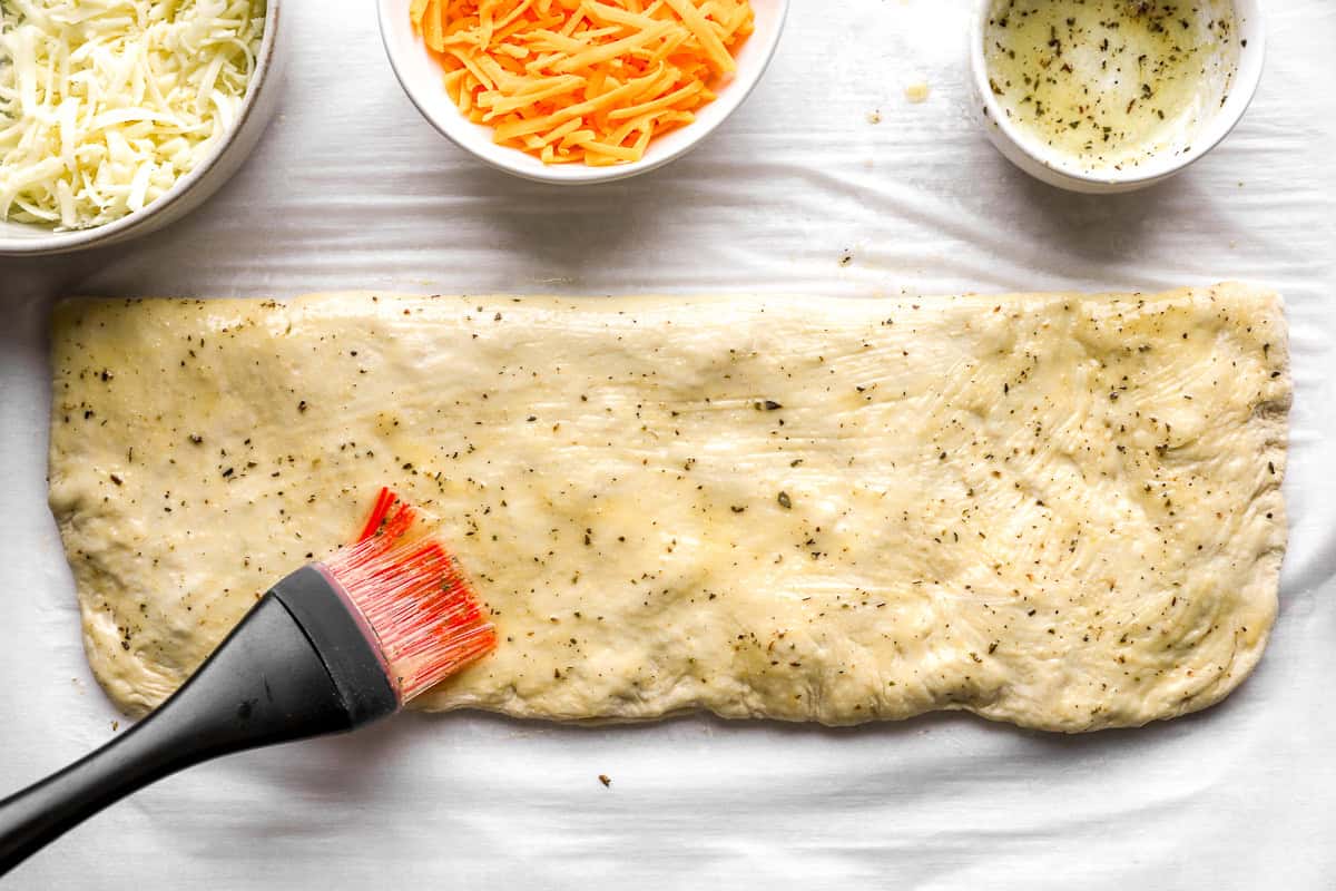 Folded and sealed stuffed cheesy bread dough brushed with garlic herb butter before slicing