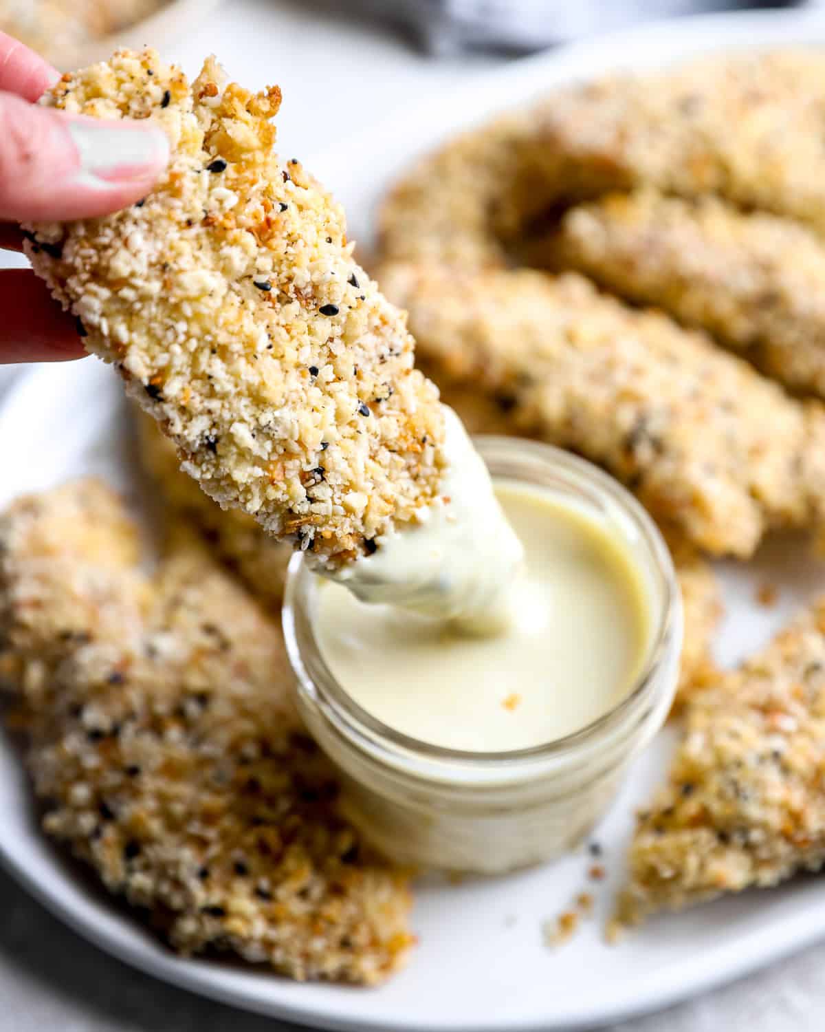 Hand dipping an everything bagel chicken strip into a bowl of creamy dipping sauce.