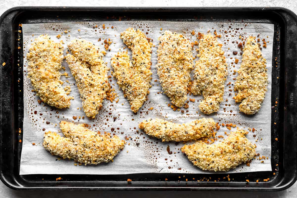 Baked everything bagel chicken tenders golden brown on a sheet pan, fresh out of the oven.