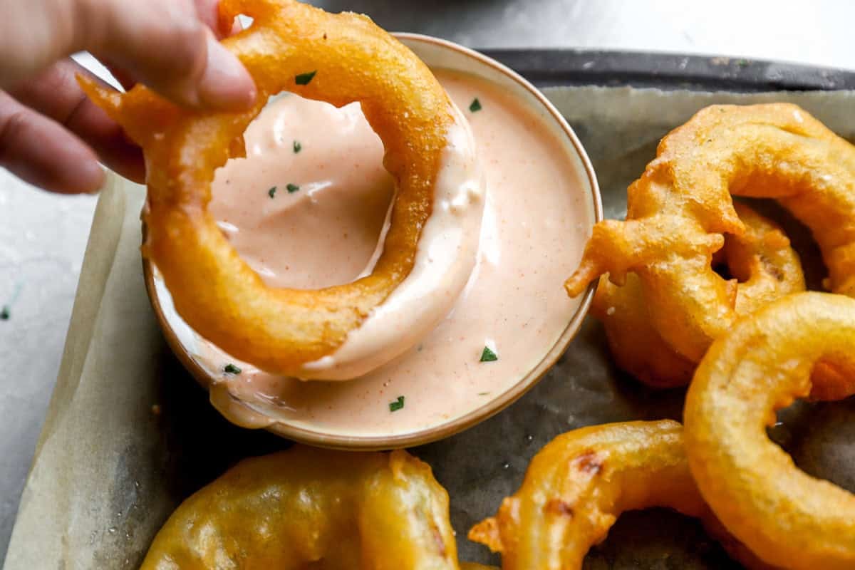 woman dipping finished onion ring into sauce