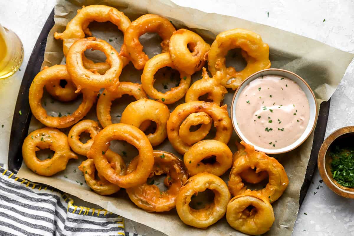 homemade onion rings served on a baking sheet with sauce