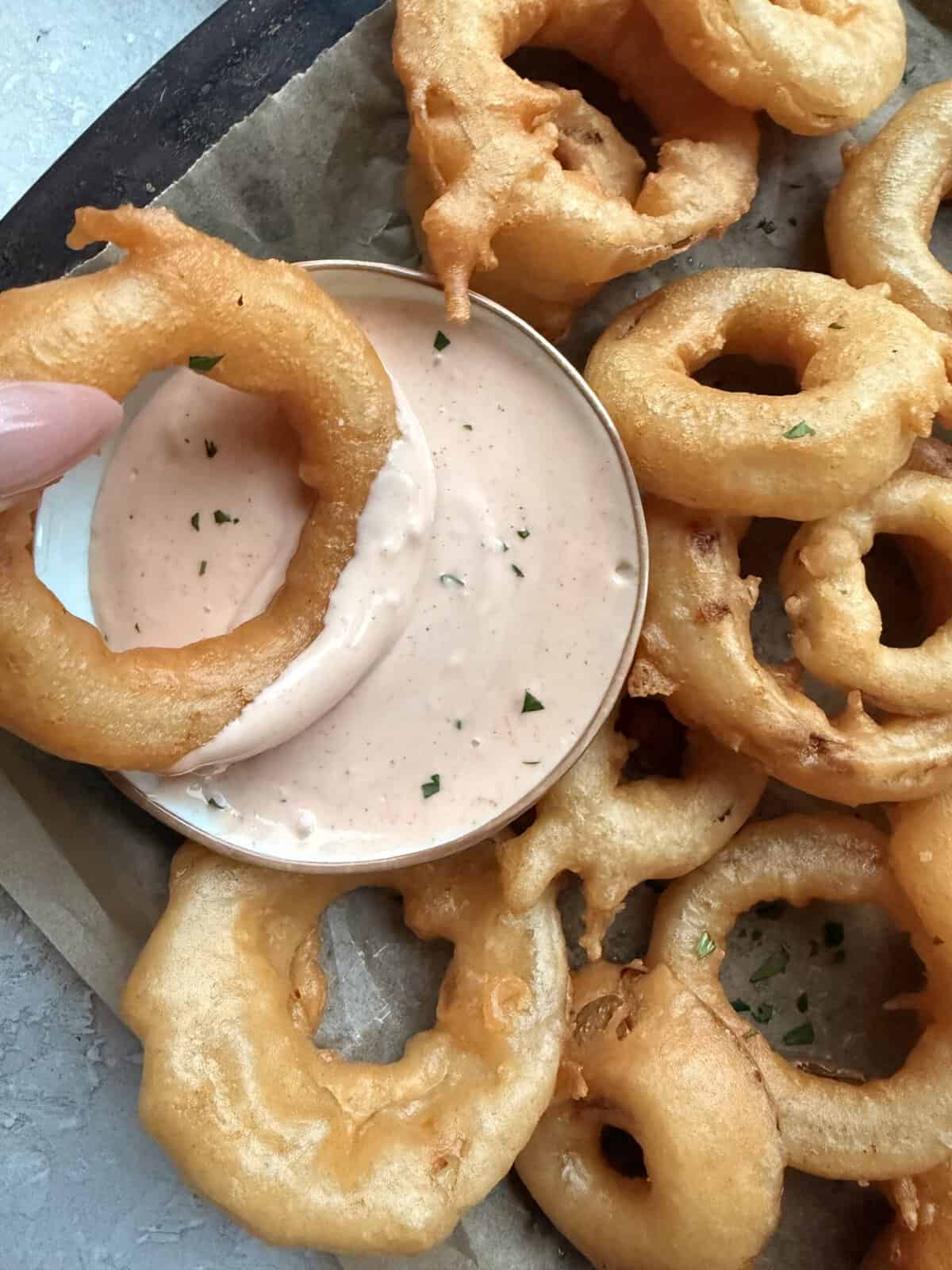 woman's hand dipping homemade onion ring in sauce