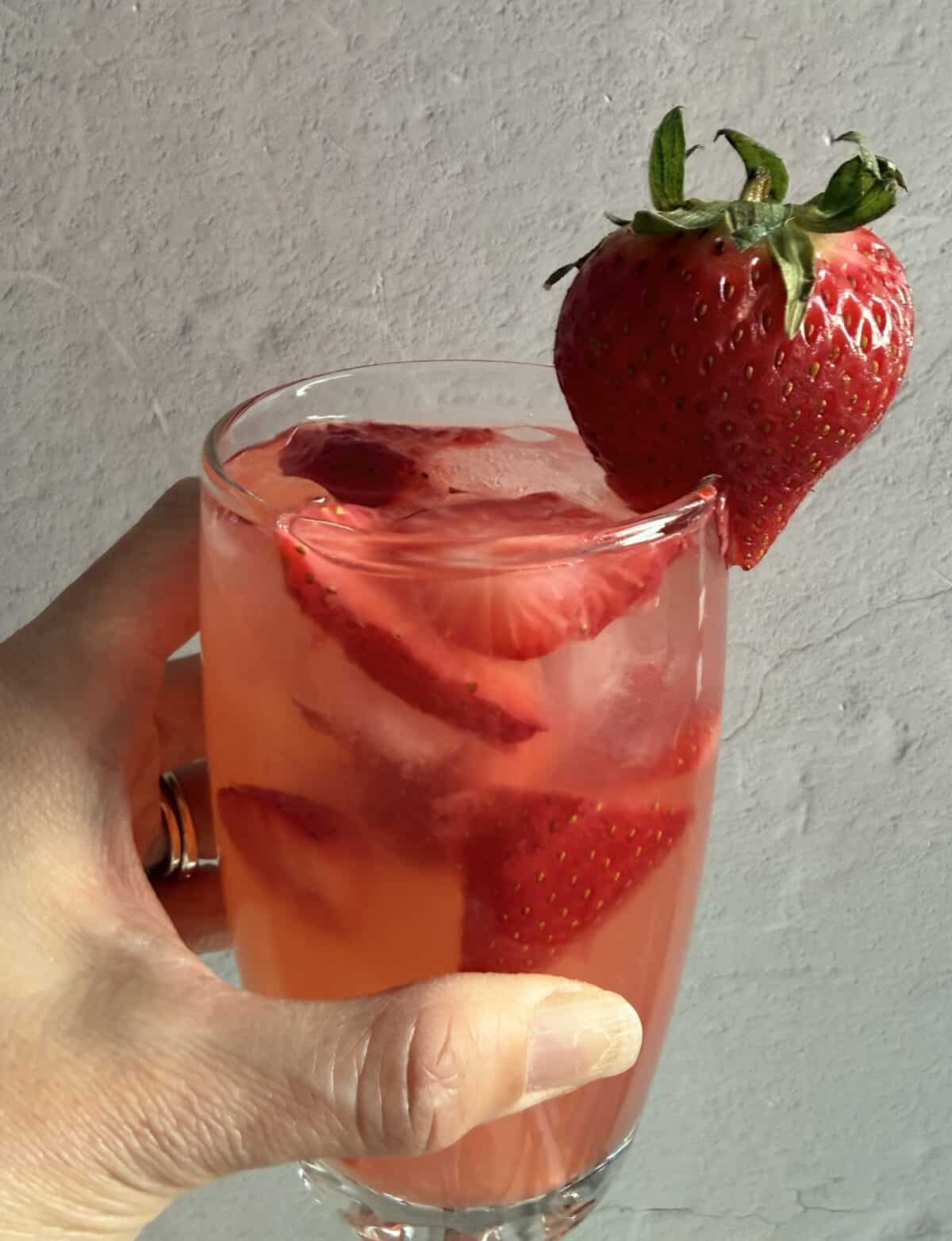 Mano che tiene un bicchiere di limonata alla fragola Red Robin con fette di fragola nella bevanda e una fragola intera sul bordo