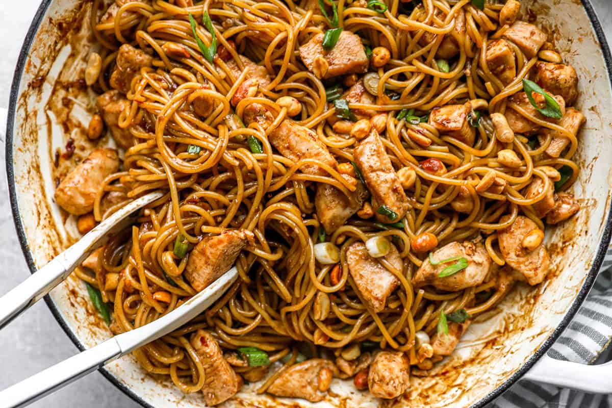 Close-up of finished kung pao spaghetti in a skillet, garnished with peanuts and green onion