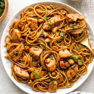 Overhead view of kung pao spaghetti on a white plate, tossed with chicken, peanuts, and green onions