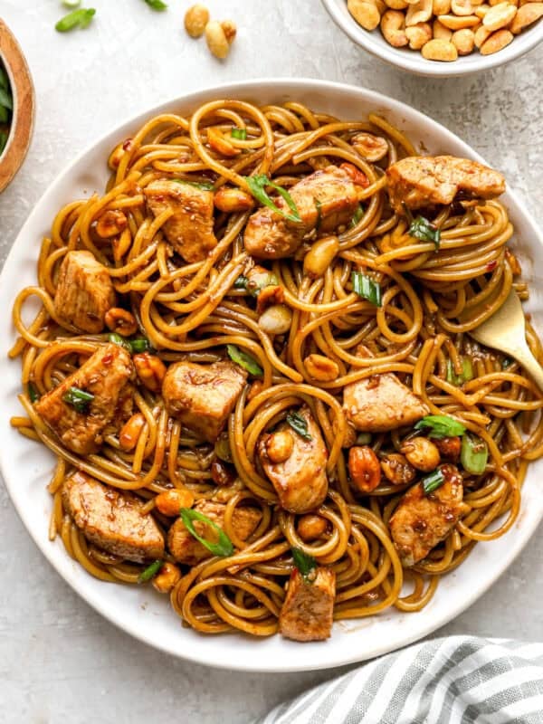 Overhead view of kung pao spaghetti on a white plate, tossed with chicken, peanuts, and green onions