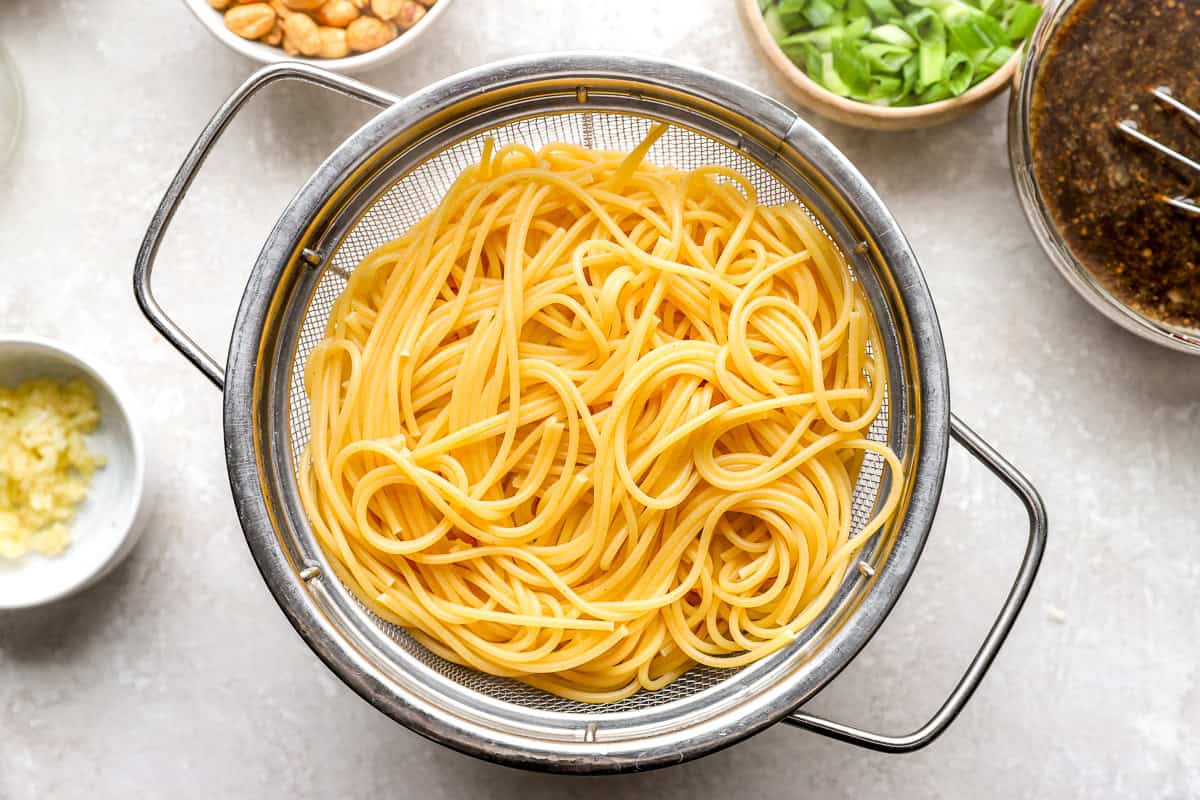 Cooked spaghetti noodles draining in a metal colander for kung pao spaghetti