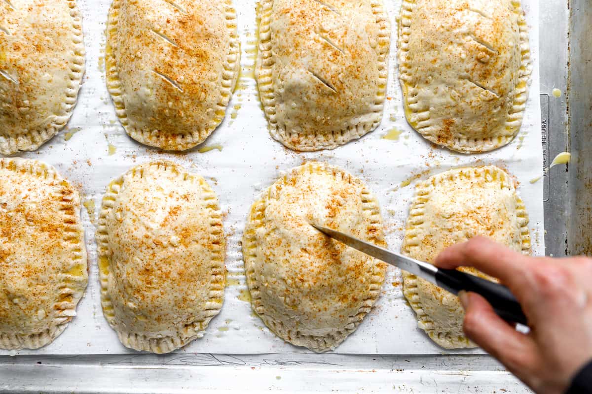 Taco seasoning sprinkled over egg-washed hot pockets while vent slits are cut into the tops.