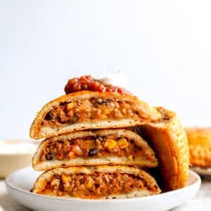 Loaded Taco Hot Pockets sliced in half and stacked on a white plate, topped with salsa and sour cream.