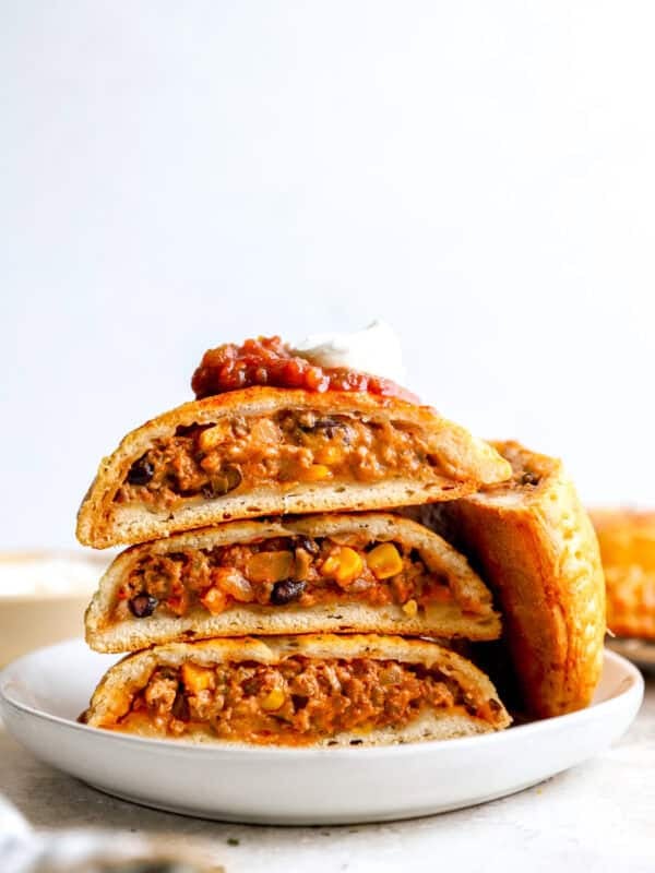 Loaded Taco Hot Pockets sliced in half and stacked on a white plate, topped with salsa and sour cream.