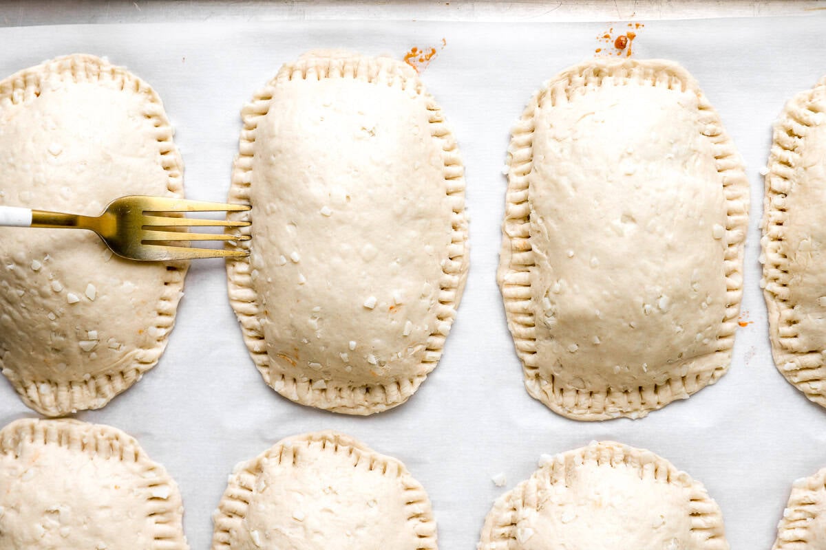 Unbaked taco hot pockets with the edges crimped shut using a fork on a parchment-lined sheet pan.