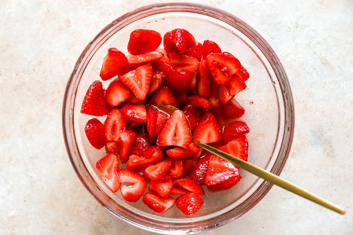 Fragole a fette macerare nello zucchero in una ciotola di vetro con un cucchiaio d'oro