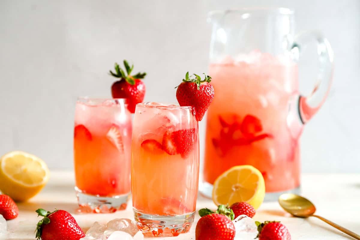 Brocca e due bicchieri di limonata alla fragola fatta in casa con fragole fresche, metà di limone e ghiaccio sparsi