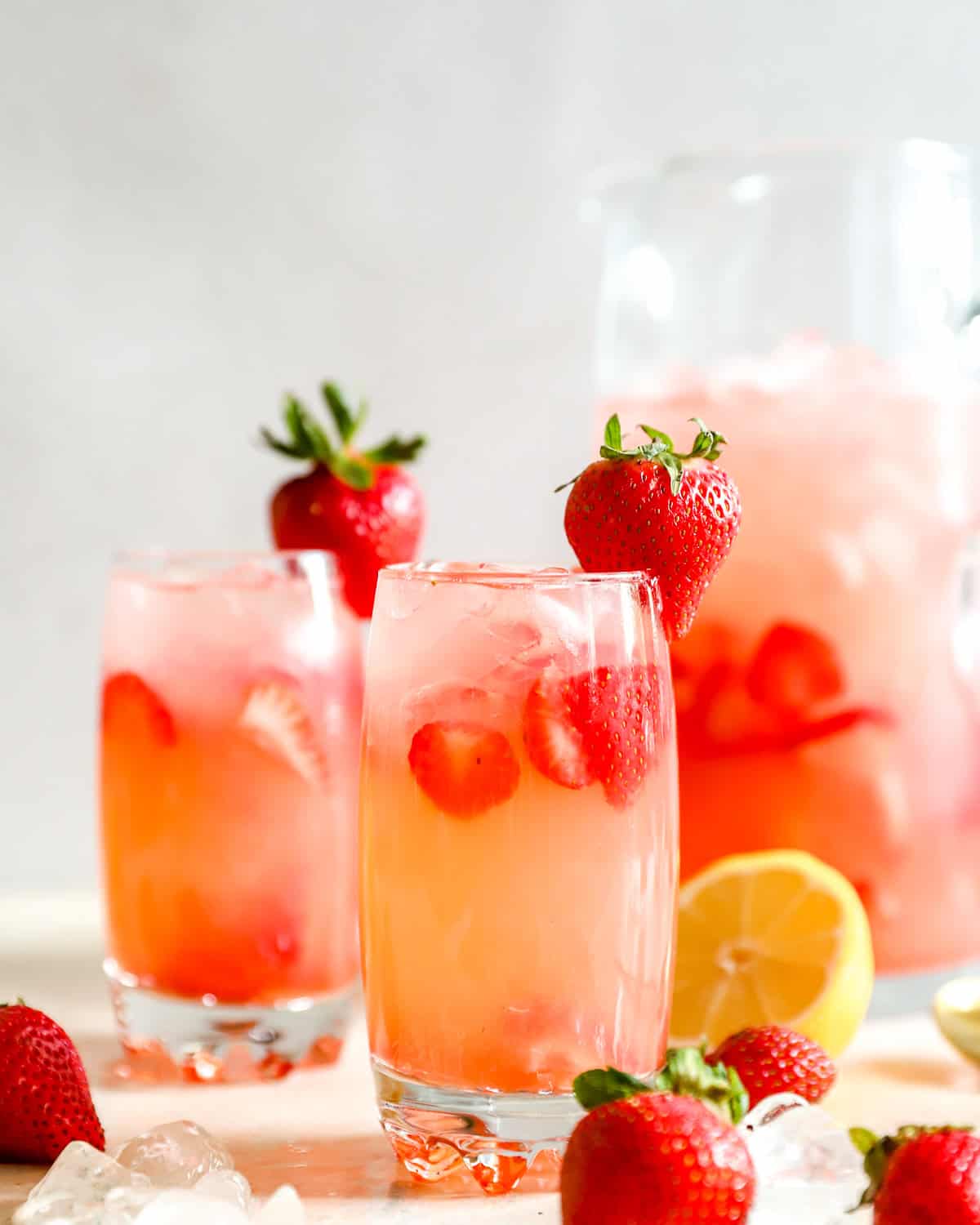 Due bicchieri di limonata alla fragola Red Robin imitante con fragole a fette e ghiaccio, con un contorno di fragole intere e una brocca dietro di loro
