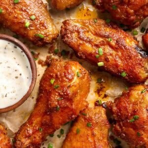 Overhead shot of crispy baked chicken wings on parchment paper with a small bowl of ranch dressing and fresh chives.
