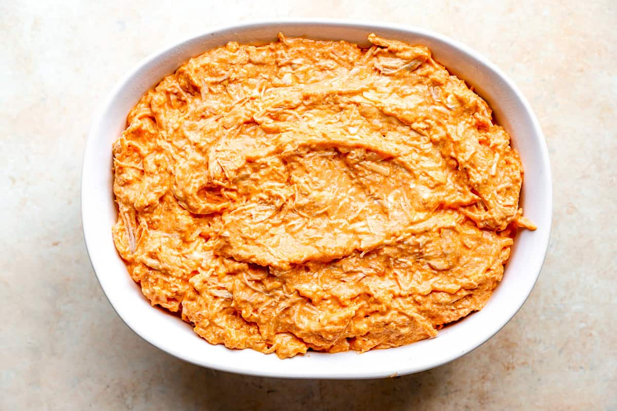 Buffalo chicken dip spread into a white baking dish, ready to go in the oven.
