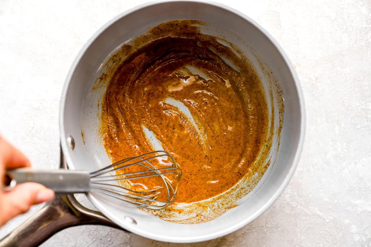 A whisk stirring butter, flour, and chili powder into a smooth roux for the green chile gravy.