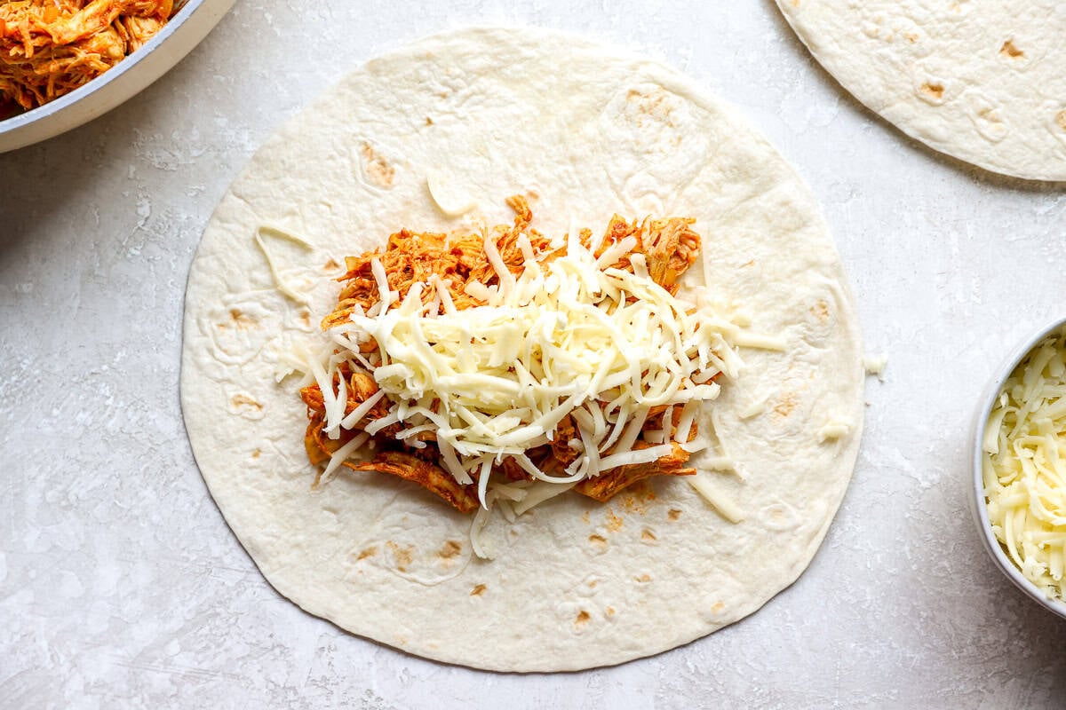 Chicken and cheese filling piled in the center of a flour tortilla before rolling.