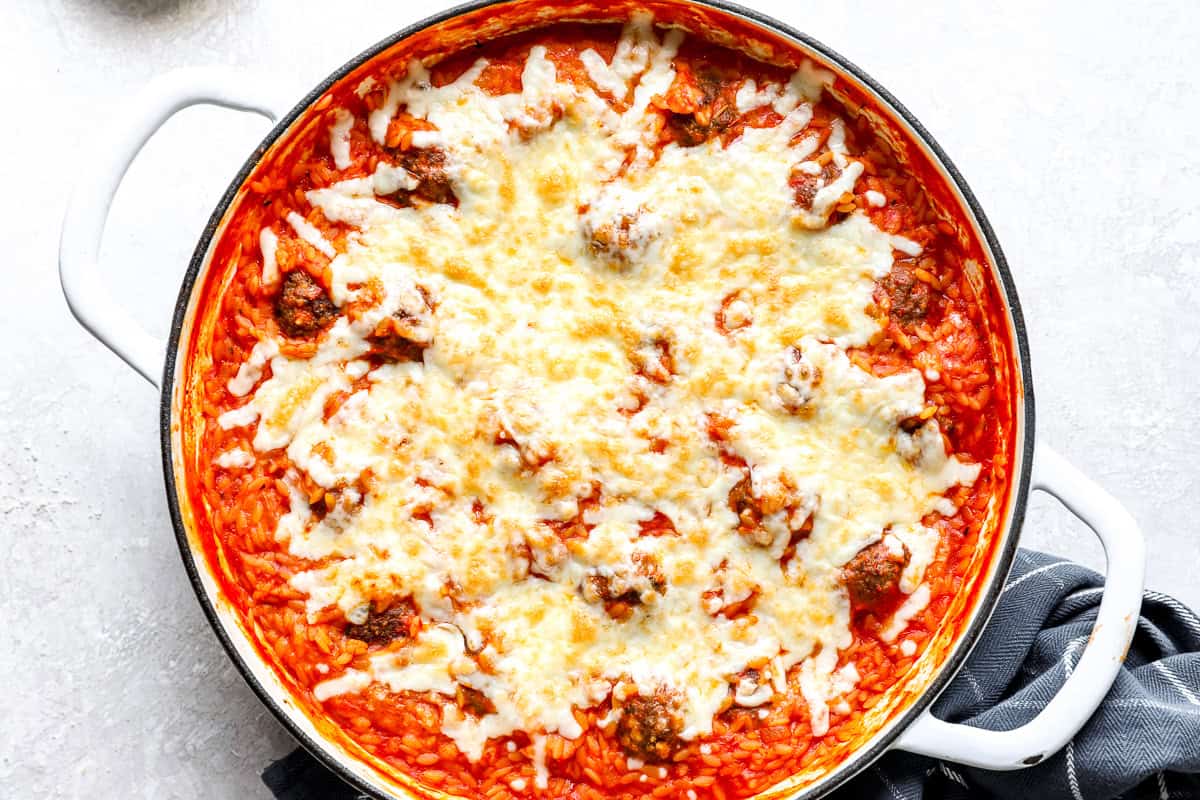 Meatball parmesan orzo topped with melted mozzarella cheese in a white skillet.