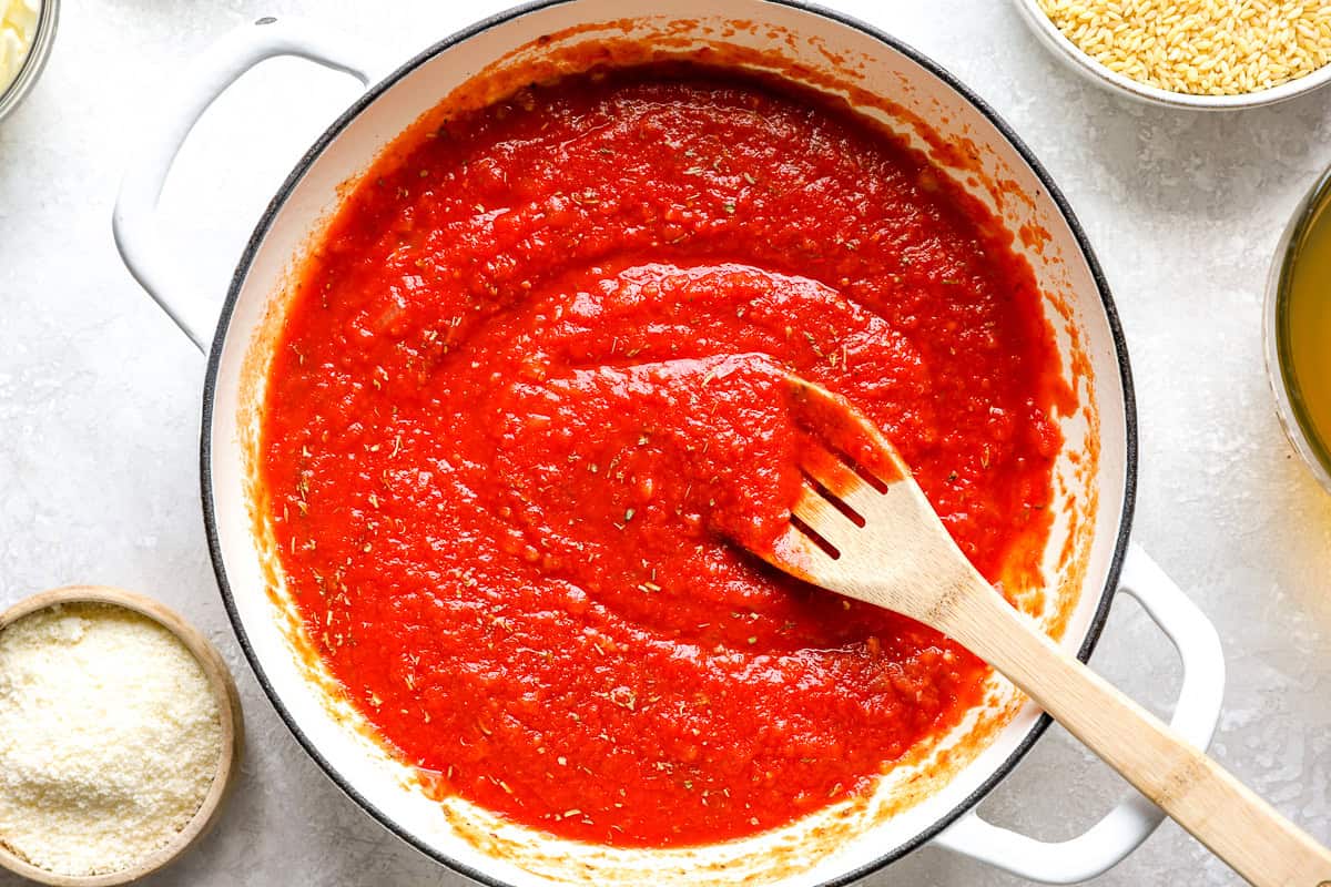 Tomato sauce simmering in a skillet, being stirred with a wooden spatula.